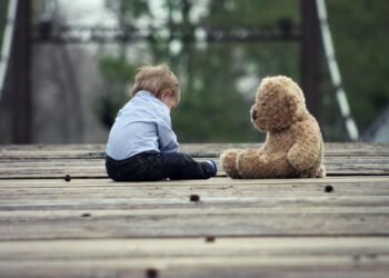 Boy Sitting With Brown Bear Plush Toy on Selective Focus Photo