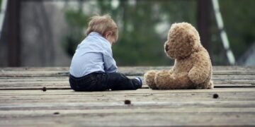 Boy Sitting With Brown Bear Plush Toy on Selective Focus Photo